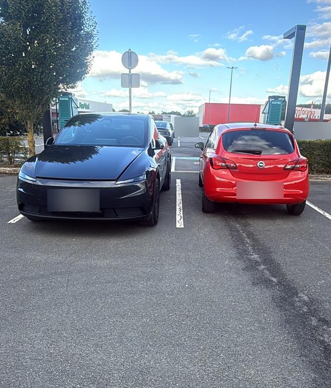 Tesla Model Y noire garée de face à côté d’une citadine rouge sur un parking